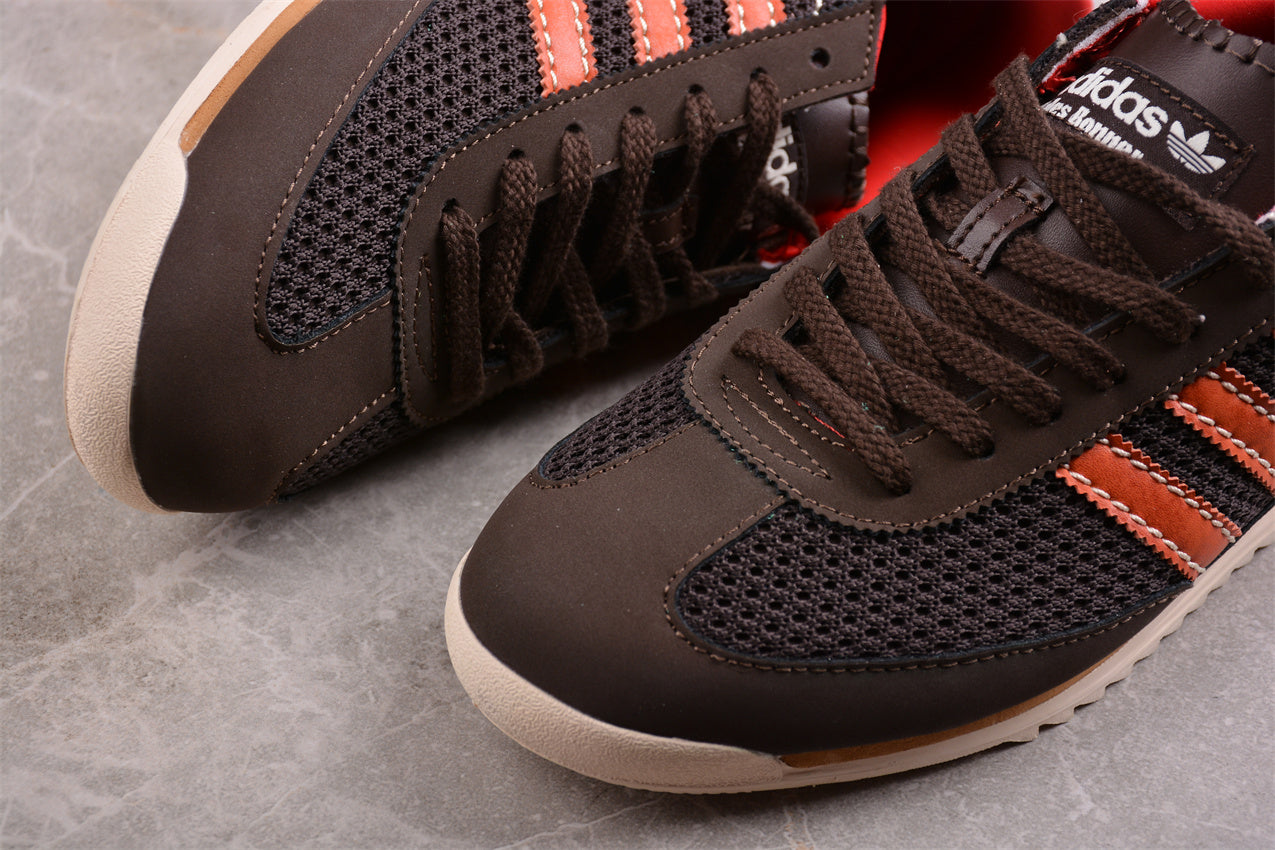 Brown Adidas sneakers with orange stripes on a gray surface