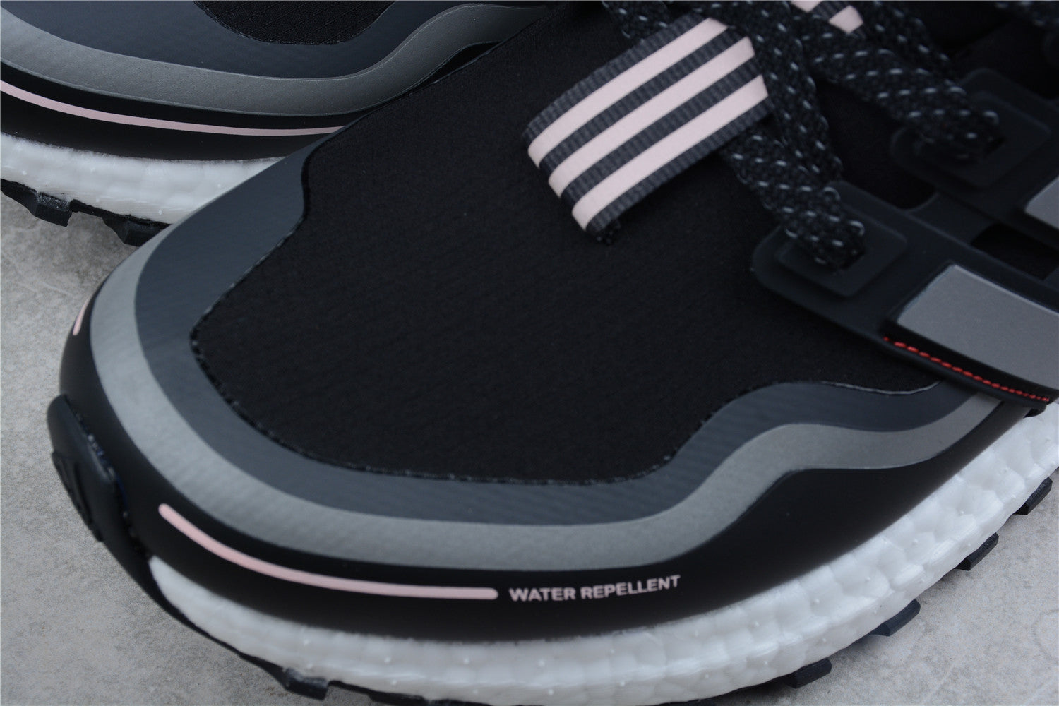Black and gray athletic shoe with water repellent feature on a concrete surface